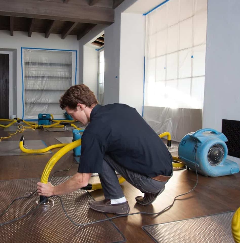 Structural drying equipment and hoses running on a water-damaged hardwood floor during a restoration job