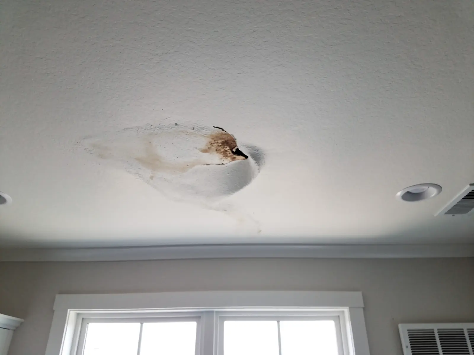 Ceiling with a water stain and slightly sagging drywall below an attic air handler