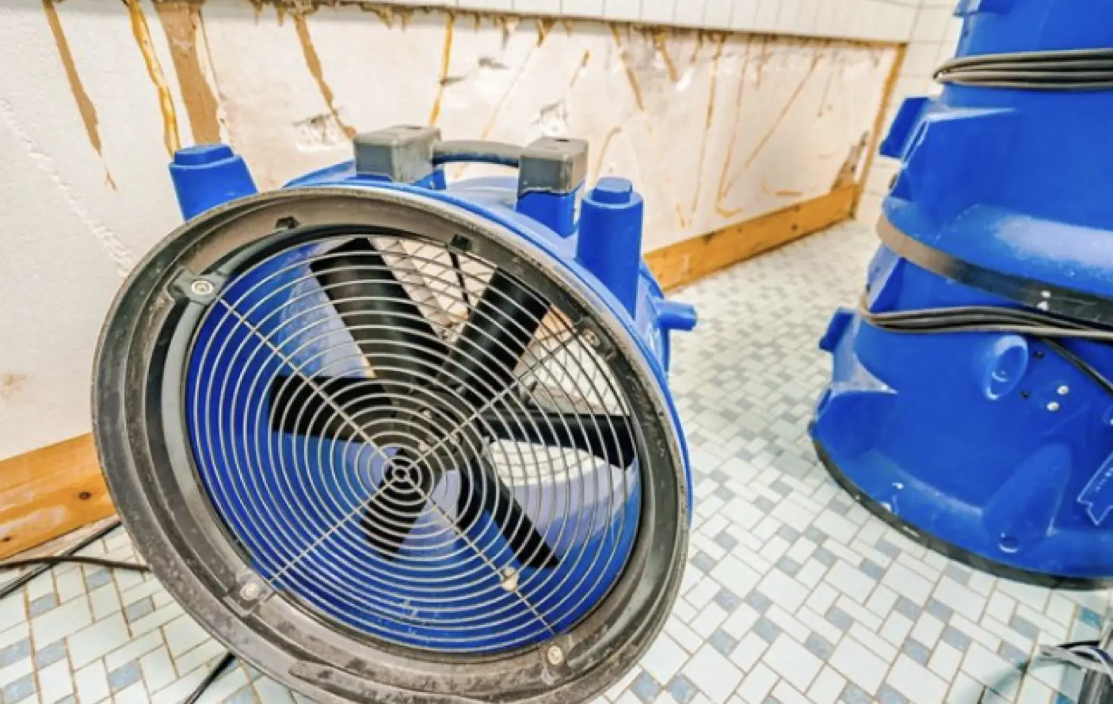 Axial fan drying a bathroom corner with a water-stained tile wall after a tub overflow
