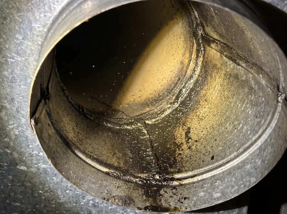 Flashlight beam inside a galvanized duct showing a dark oily soot film