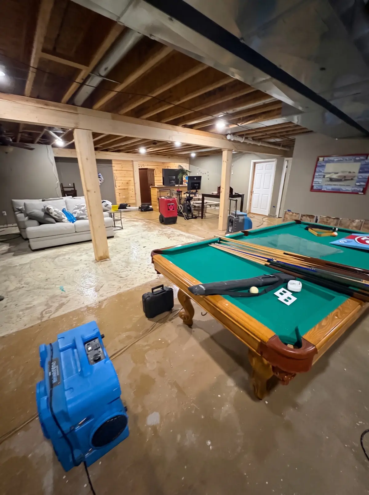 Finished basement with a pool table, carpet removed and drying equipment running