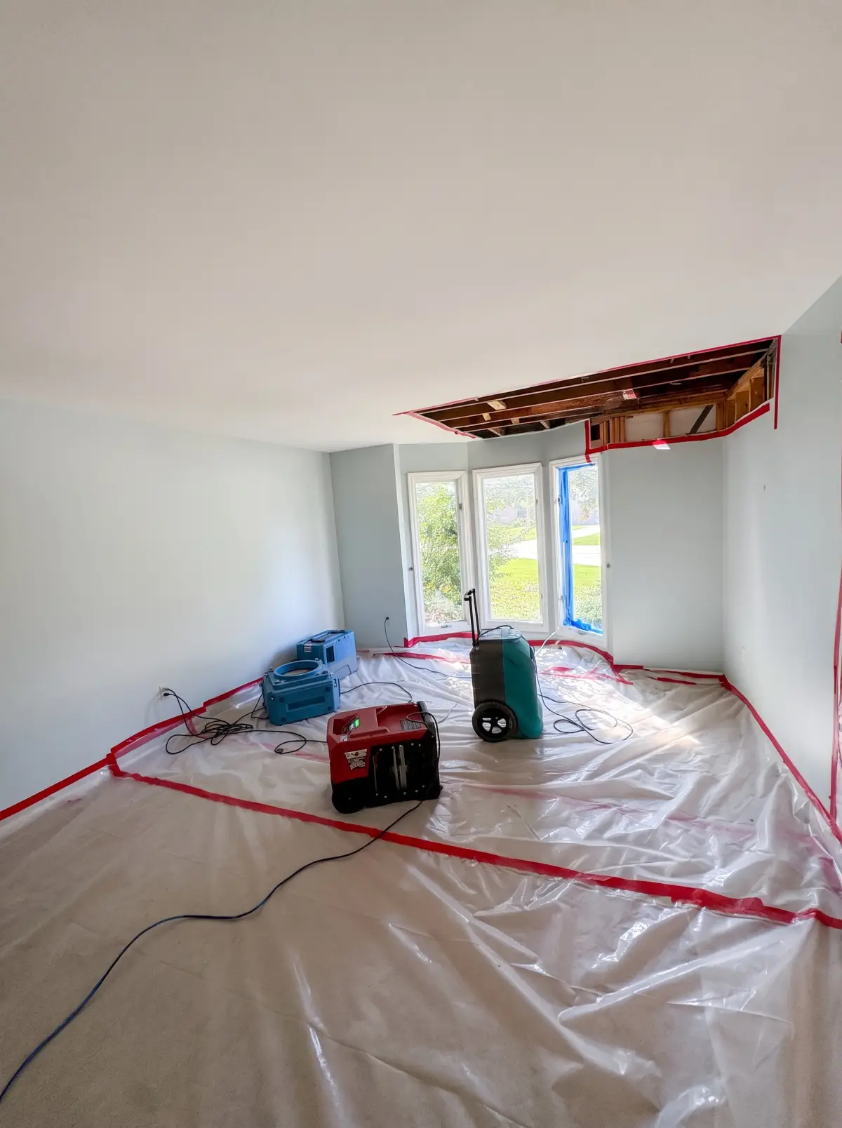 Room with an opened ceiling, plastic over the floor and drying equipment running