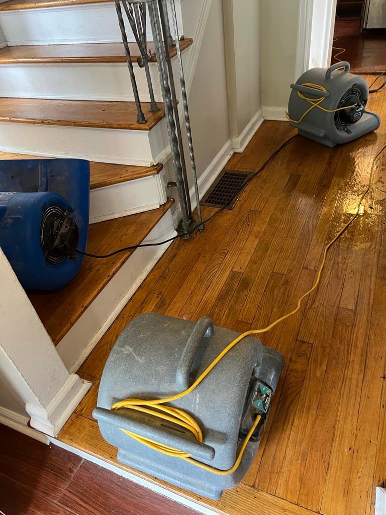 Air movers running on hardwood flooring at the foot of a staircase during a structural dry-out