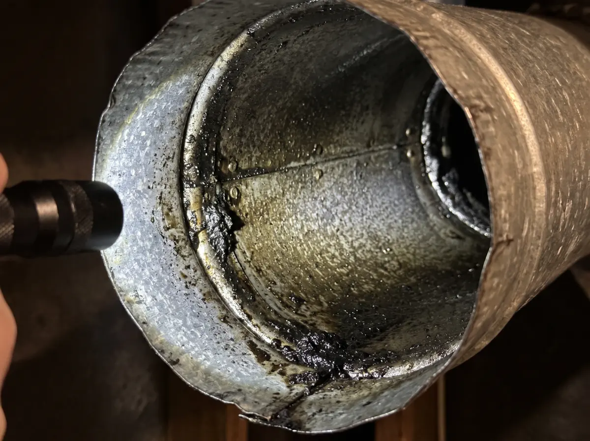 Inside a metal heating duct coated with an oily black soot residue