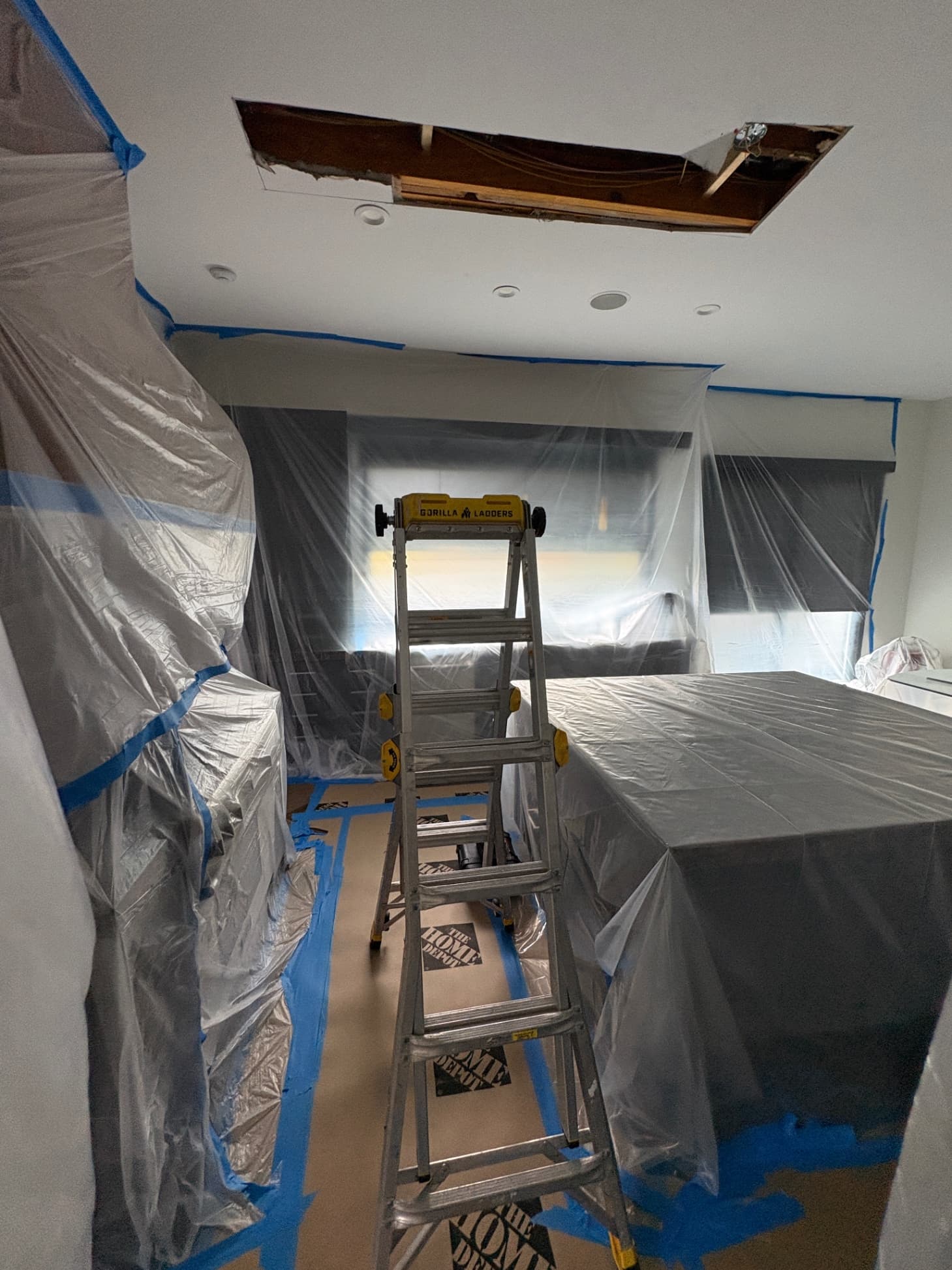 A kitchen sealed in plastic containment with a ladder under an opened ceiling, before water-damaged drywall is removed